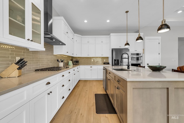 kitchen featuring light wood finished floors, a sink, stainless steel appliances, tasteful backsplash, and wall chimney exhaust hood
