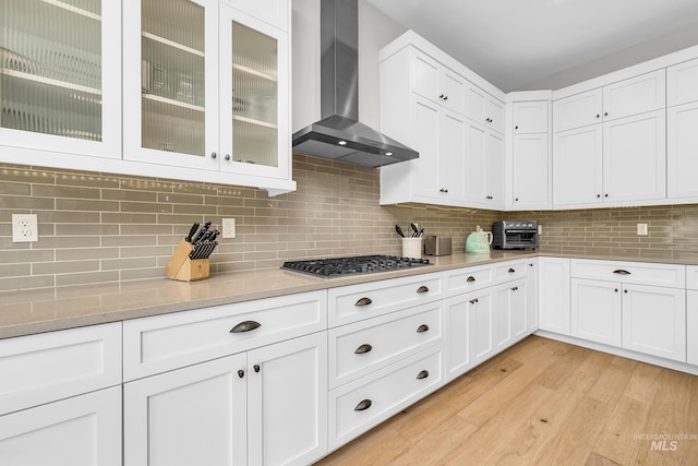 kitchen featuring stainless steel gas cooktop, decorative backsplash, wall chimney range hood, white cabinets, and light wood-type flooring