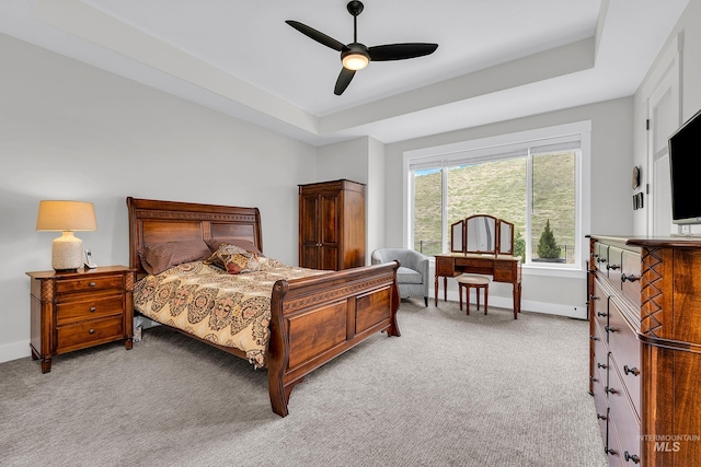 bedroom with ceiling fan, baseboards, light colored carpet, and a tray ceiling