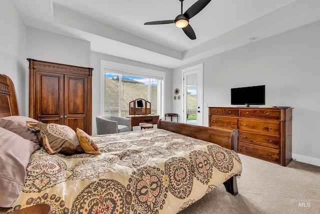 carpeted bedroom featuring access to exterior, ceiling fan, a tray ceiling, and baseboards