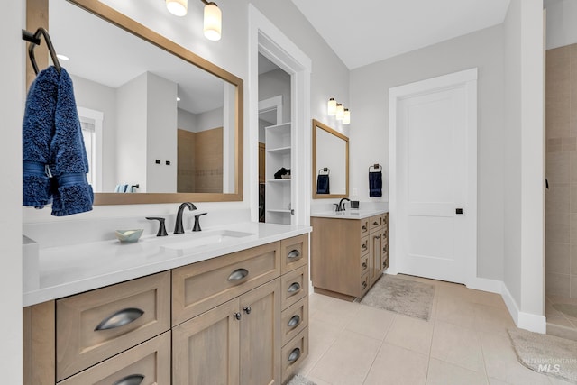 bathroom featuring tile patterned floors, two vanities, a tile shower, and a sink