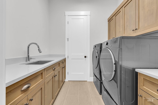 laundry area featuring light tile patterned floors, washing machine and dryer, cabinet space, and a sink