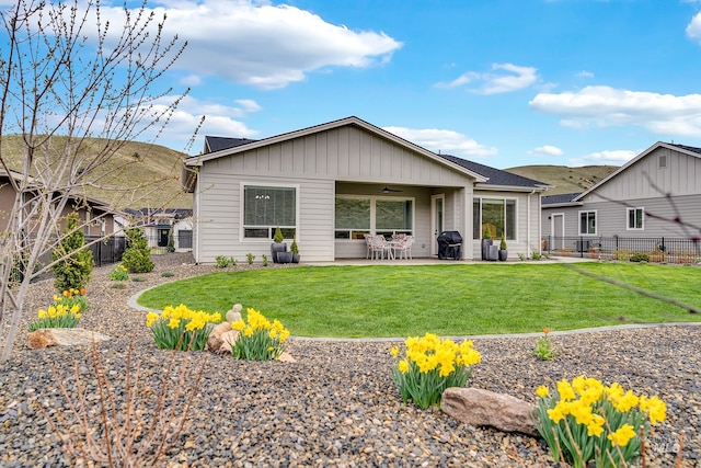 rear view of house with board and batten siding, a patio area, ceiling fan, a lawn, and a fenced backyard