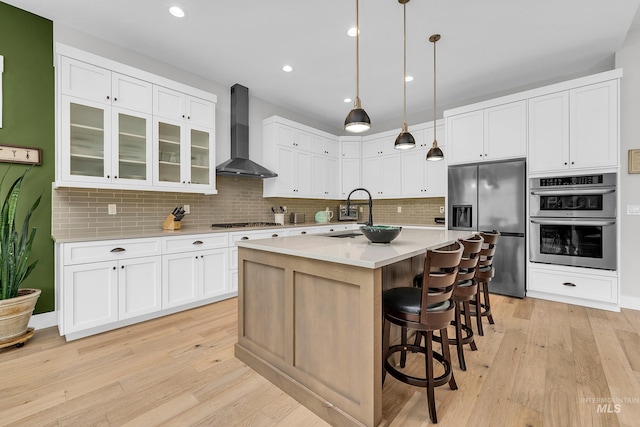 kitchen with light wood-style flooring, stainless steel appliances, wall chimney range hood, and a sink