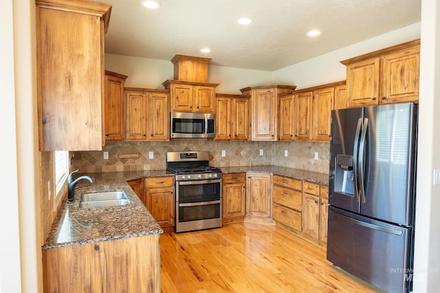 6023 S Augustine Ave, Boise, ID 83709 - kitchen with appliances with stainless steel finishes, a sink, brown cabinets, light wood-style floors, and dark stone counters