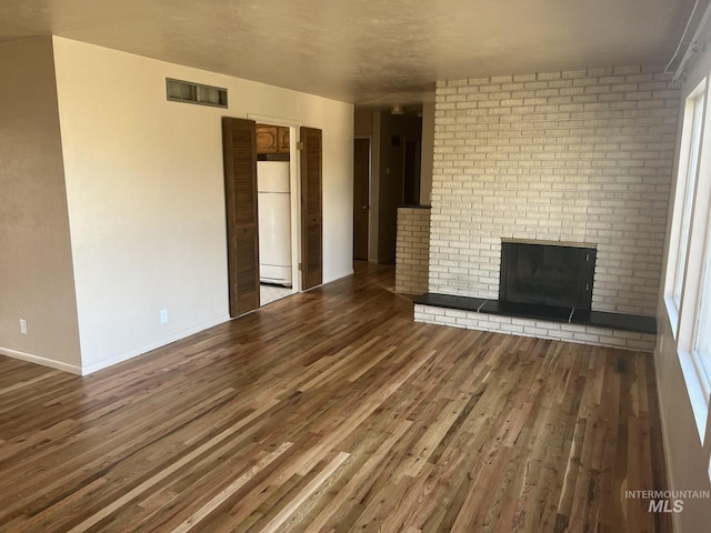 unfurnished living room with dark hardwood / wood-style flooring and a brick fireplace