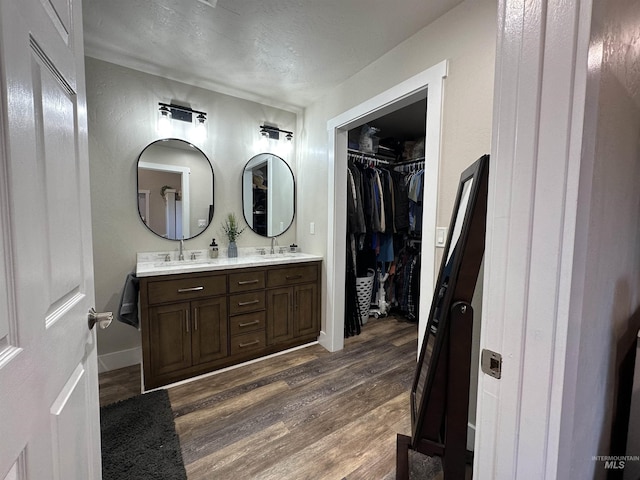 bathroom featuring double vanity, wood finished floors, baseboards, a walk in closet, and a sink