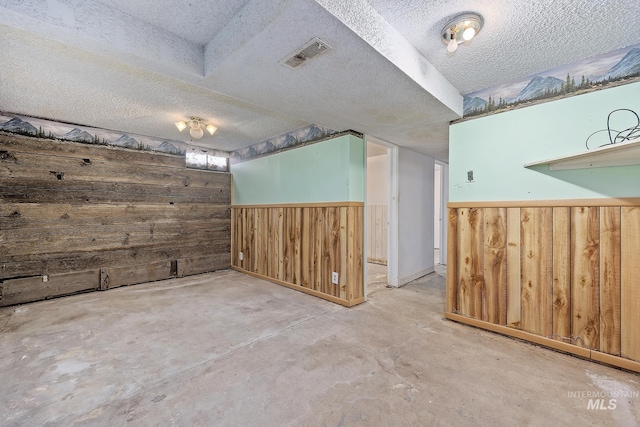 spare room featuring wooden walls, concrete flooring, and a textured ceiling