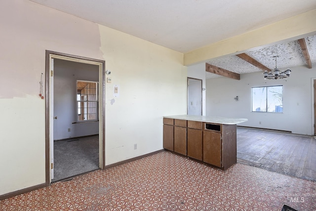 kitchen with a notable chandelier, beam ceiling, kitchen peninsula, and a wealth of natural light