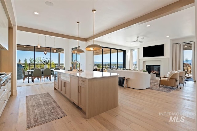 kitchen with a ceiling fan, plenty of natural light, a glass covered fireplace, light wood-type flooring, and decorative light fixtures