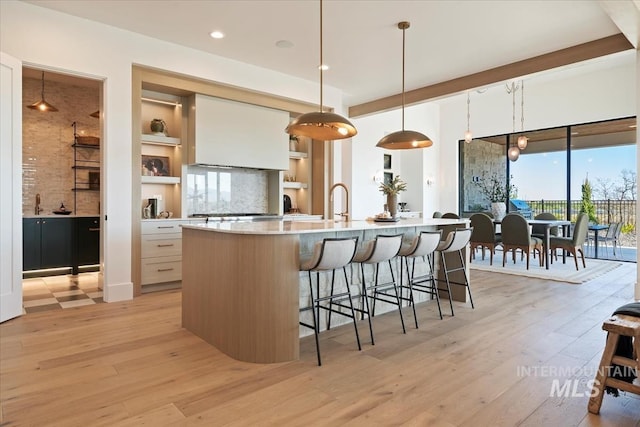 kitchen featuring open shelves, a large island with sink, a breakfast bar, light wood finished floors, and light countertops