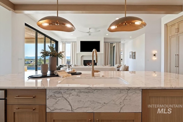 kitchen featuring a sink, open floor plan, light stone counters, a lit fireplace, and hanging light fixtures