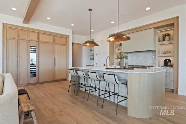 kitchen with recessed lighting, light brown cabinetry, a large island, a kitchen bar, and light wood-style flooring