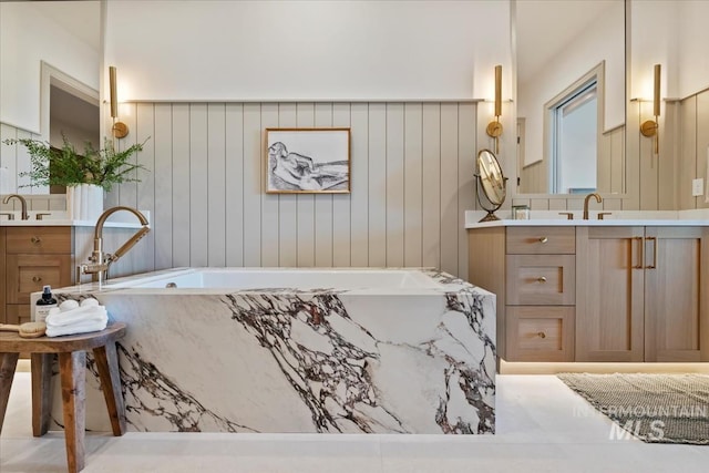 full bath featuring two vanities, a tub with marble appearance, and a sink