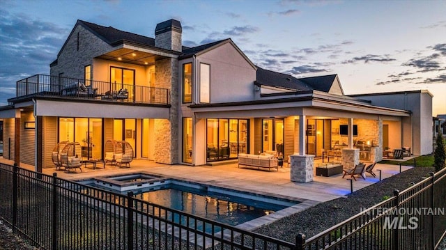 back of property featuring a balcony, a chimney, outdoor lounge area, stone siding, and a patio