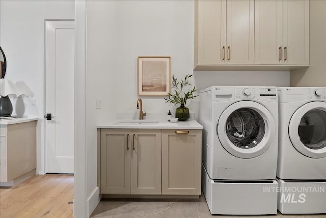 clothes washing area featuring cabinet space, light wood-style floors, a sink, and washer and clothes dryer