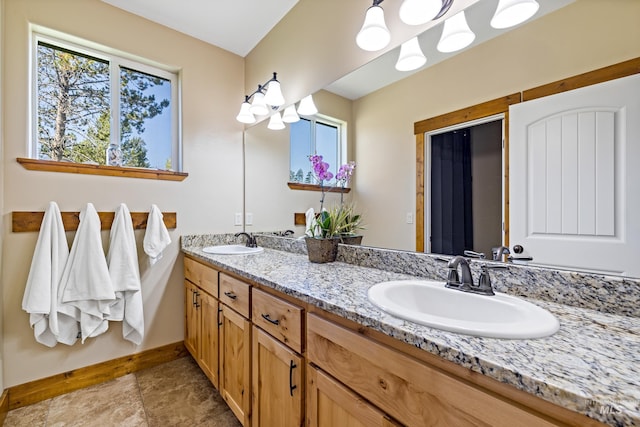 bathroom with a sink, double vanity, baseboards, and a chandelier
