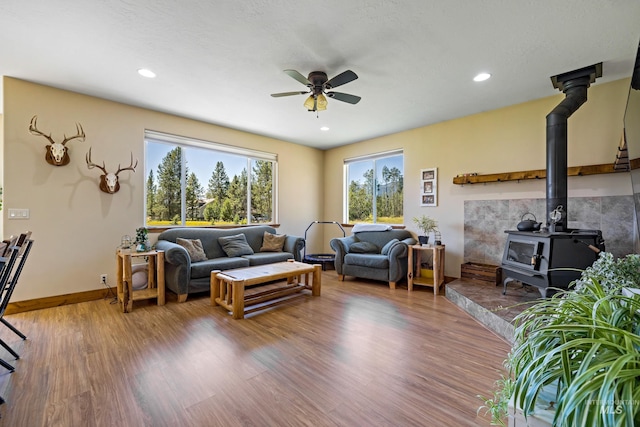 living room featuring wood finished floors, baseboards, ceiling fan, a wood stove, and recessed lighting
