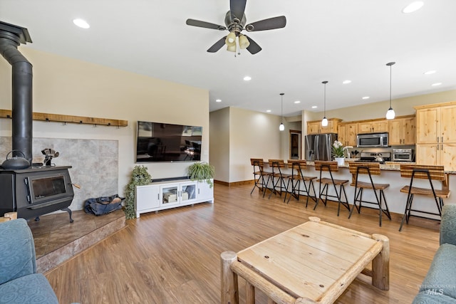 living room with a wood stove, ceiling fan, light wood-type flooring, and a toaster