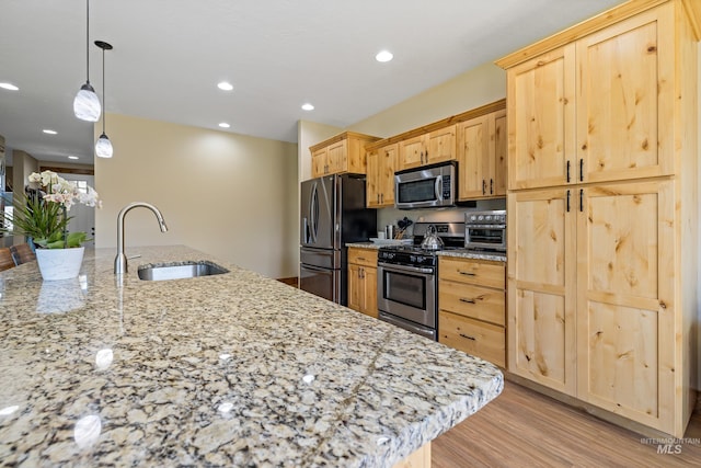 kitchen with a sink, stainless steel appliances, light brown cabinets, and light wood-style flooring