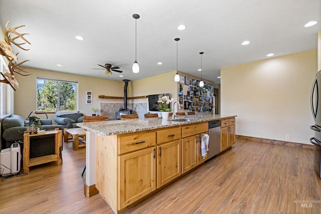 kitchen featuring a sink, open floor plan, light wood-type flooring, stainless steel dishwasher, and a wood stove