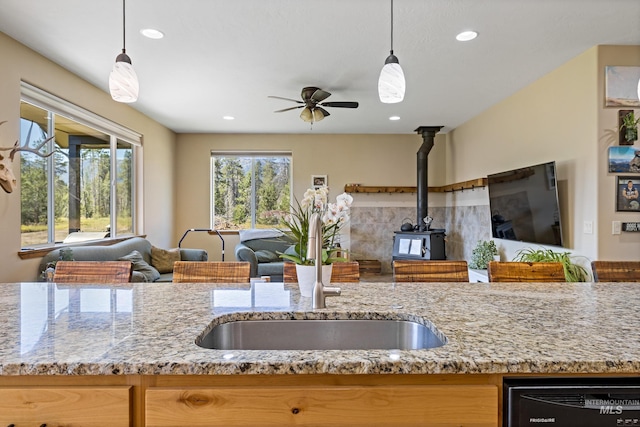 kitchen with a ceiling fan, a sink, black dishwasher, open floor plan, and a wood stove