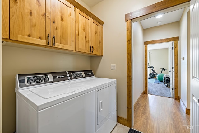 clothes washing area featuring cabinet space, independent washer and dryer, light wood-style flooring, and baseboards