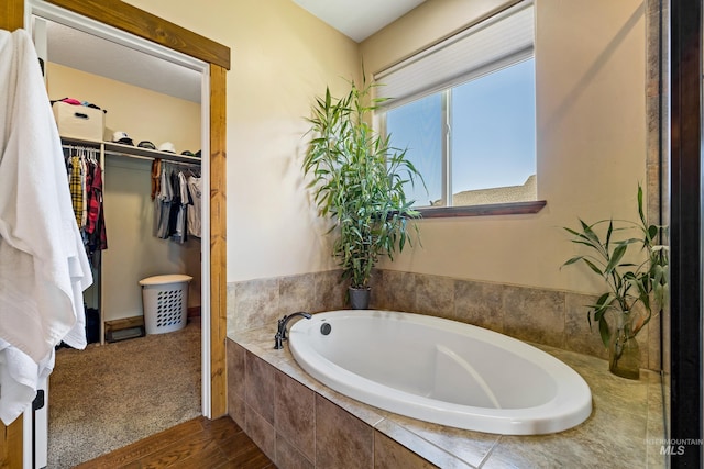 full bathroom with a garden tub, wood finished floors, and a walk in closet