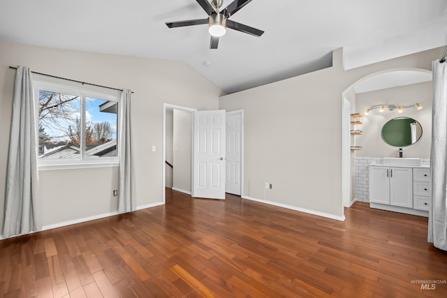 unfurnished bedroom with ceiling fan, dark wood-type flooring, baseboards, vaulted ceiling, and ensuite bath