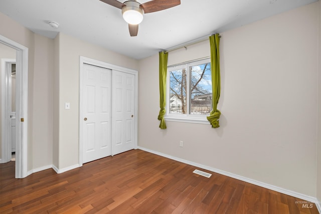 unfurnished bedroom featuring a ceiling fan, visible vents, baseboards, a closet, and dark wood finished floors