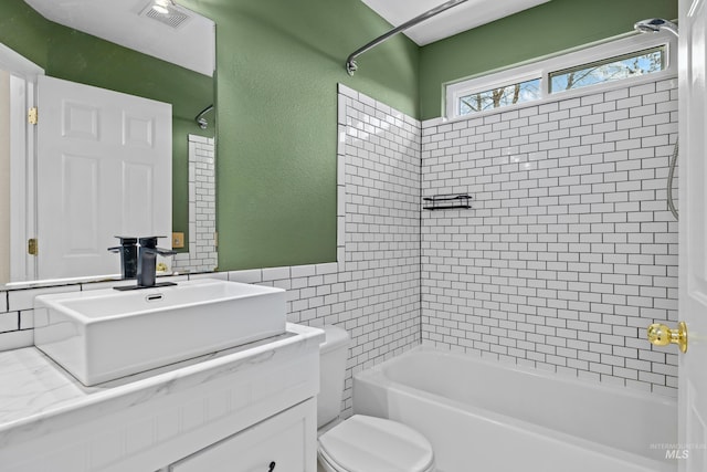 full bathroom with toilet, visible vents, vanity, tile walls, and washtub / shower combination