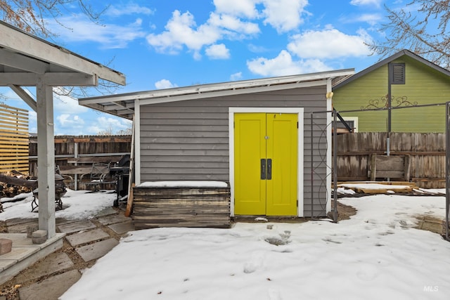 snow covered structure featuring an outbuilding, a storage unit, and fence