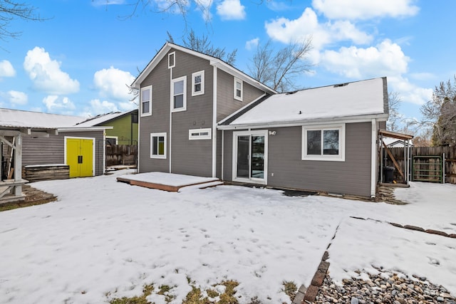 snow covered house with a shed, fence, a wooden deck, and an outdoor structure