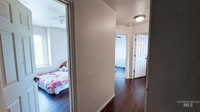 corridor with a textured ceiling, a textured wall, baseboards, and dark wood finished floors