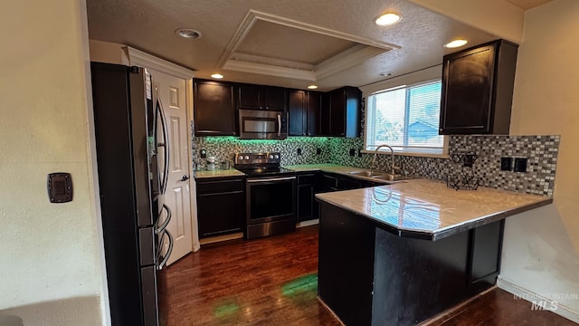 kitchen featuring a sink, a peninsula, backsplash, a raised ceiling, and appliances with stainless steel finishes