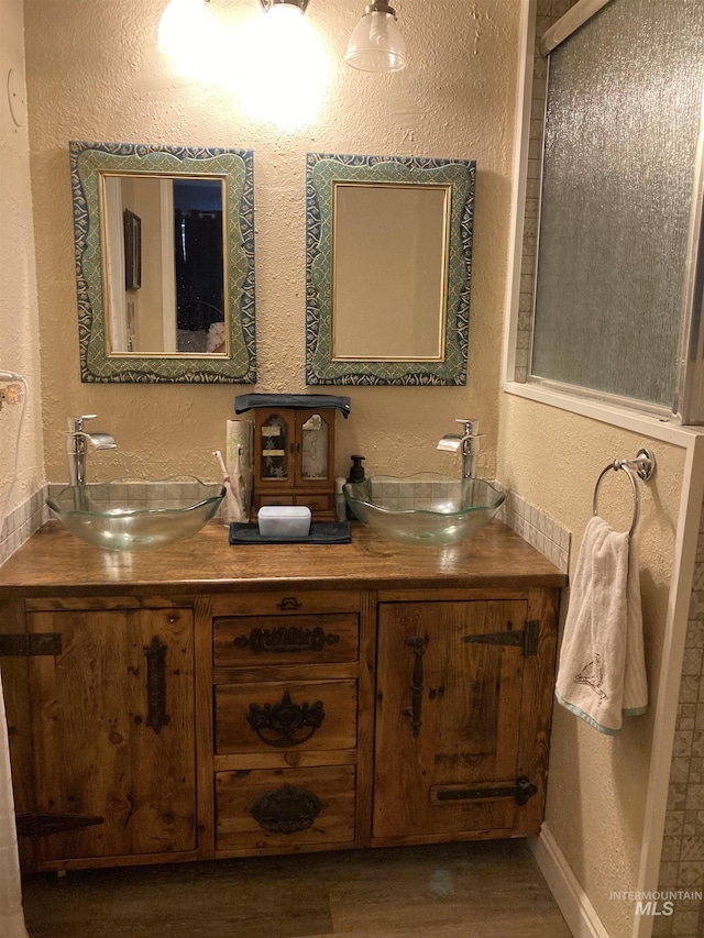 bathroom featuring double vanity, a textured wall, and a sink