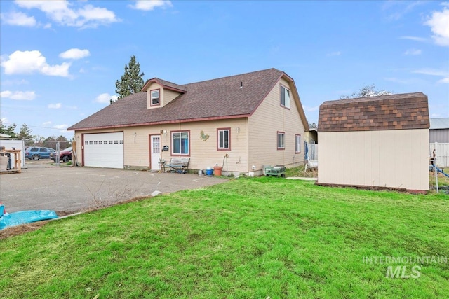 back of house with roof with shingles, a storage unit, a garage, aphalt driveway, and a lawn