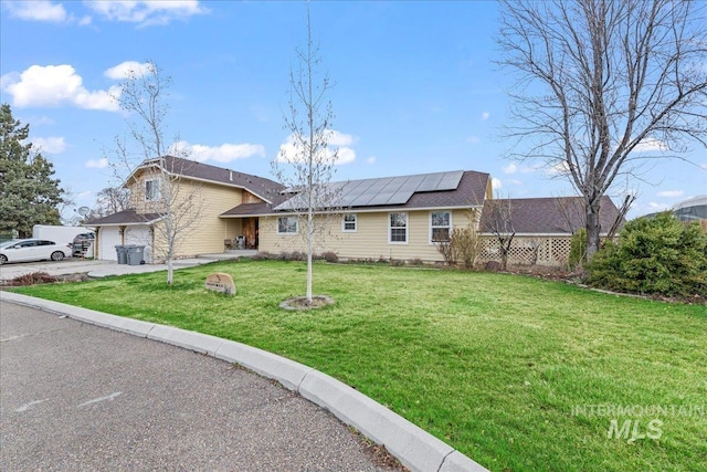 split level home with roof mounted solar panels, driveway, and a front lawn