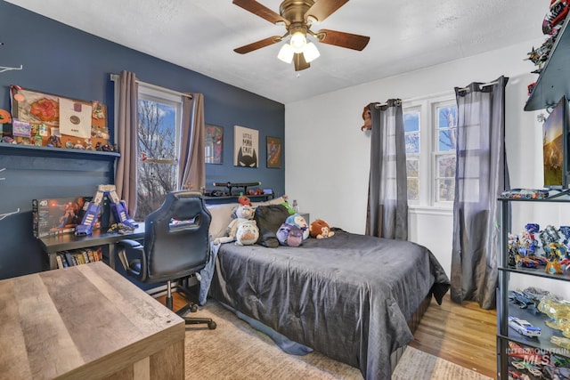 bedroom featuring a textured ceiling, ceiling fan, multiple windows, and wood finished floors