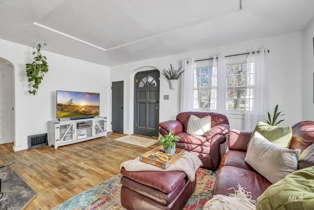 living room with arched walkways, wood finished floors, and visible vents