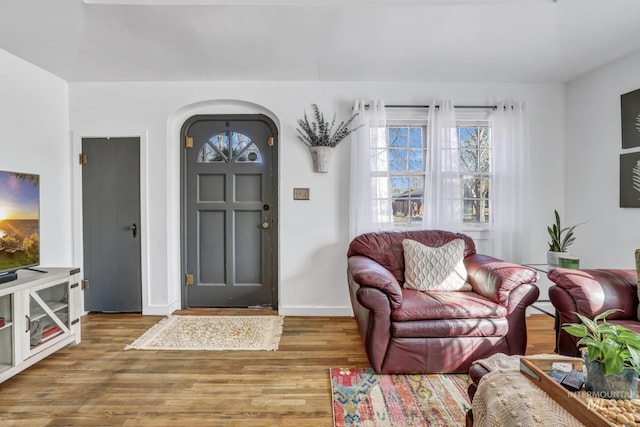 entrance foyer with arched walkways, baseboards, and wood finished floors