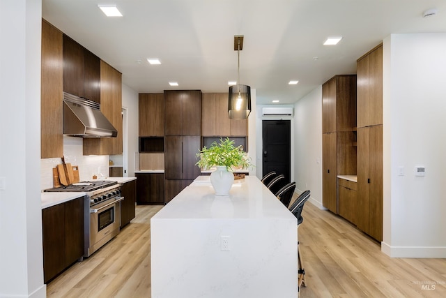 kitchen featuring stainless steel range, decorative backsplash, pendant lighting, and light hardwood / wood-style flooring