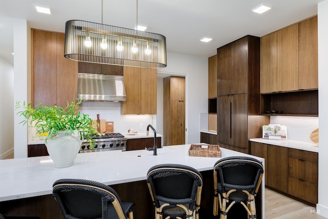 kitchen featuring decorative light fixtures, a kitchen bar, tasteful backsplash, light hardwood / wood-style floors, and stove