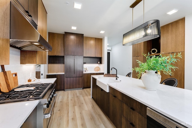 kitchen featuring extractor fan, light hardwood / wood-style floors, high end stove, hanging light fixtures, and sink