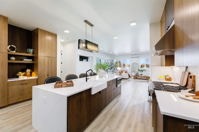 kitchen with wall chimney exhaust hood, sink, hanging light fixtures, a large island, and light hardwood / wood-style flooring