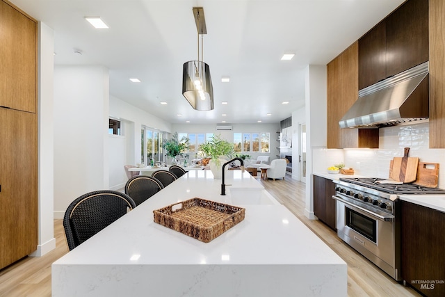 kitchen featuring decorative light fixtures, sink, an island with sink, and high end stove