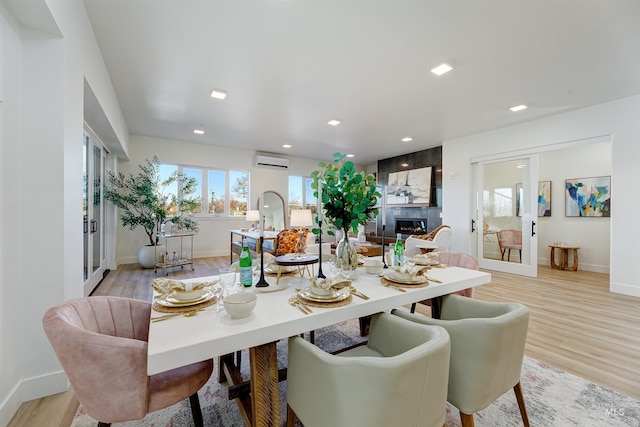 dining space with a premium fireplace, a wall mounted AC, and light hardwood / wood-style flooring