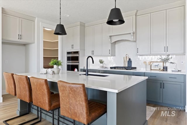 8447 W Happy Day Dr, Meridian, ID 83646 - kitchen with a sink, stainless steel appliances, light wood-style flooring, an island with sink, and hanging light fixtures