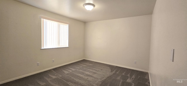 spare room with dark carpet and baseboards