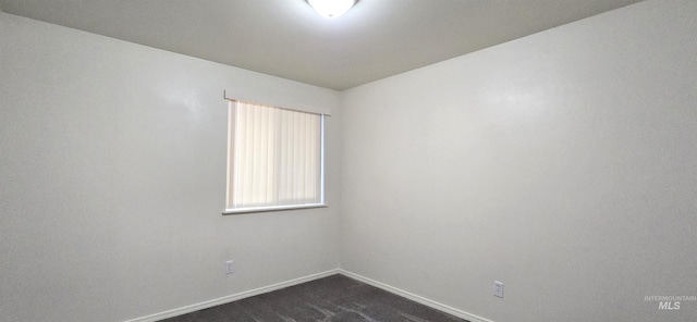 unfurnished room featuring baseboards and dark carpet